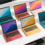 Five budget laptops open and arranged side by side on a clean white desk